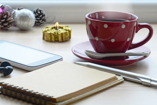 Foto av en kaffekopp, ett anteckningsblock med penna och en mobiltelefon.