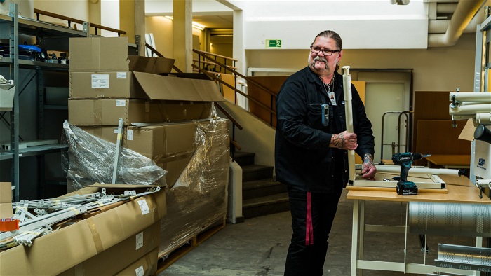 Mikael Bergström står i möbelförrådet och skruvar ihop ett bord. Foto.