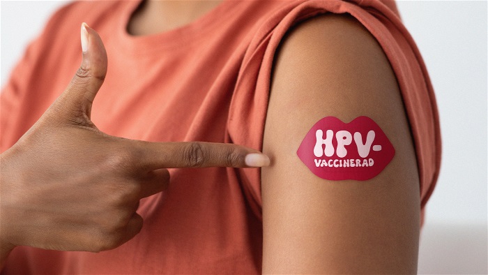 Kvinna pekar på överarm med plåster där det står "HPV-vaccinerad".