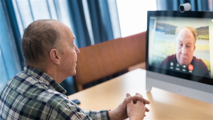 Äldre man sitter framför en dator och har ett videosamtal med vårdpersonal. Foto.