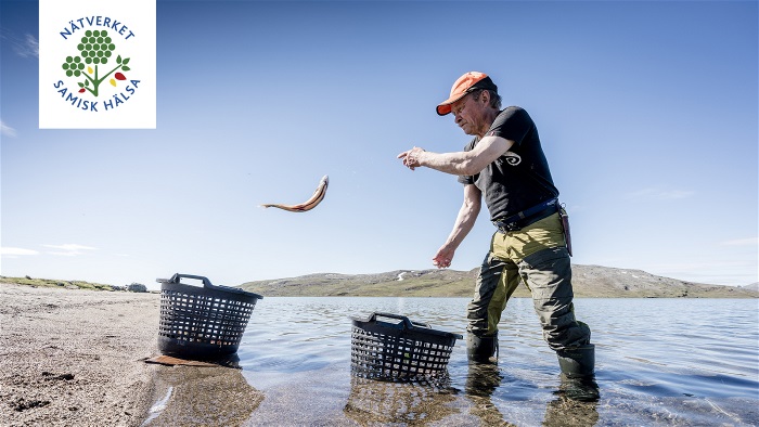 Man står utomhus i vatten och kastar upp en fisk på land. Foto.