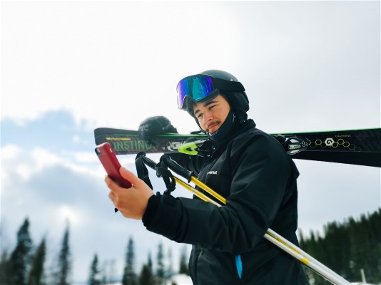 Man med slalomskidor som tittar på sin mobiltelefon.