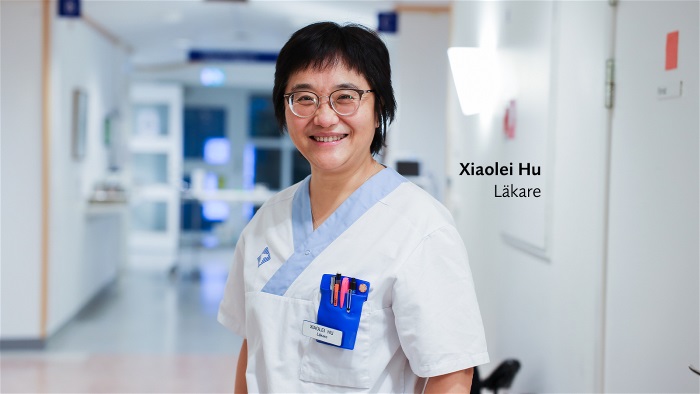 Xiaolei Hu står i korridor, har på sig vårdkläder, ler och tittar in i kameran. Foto