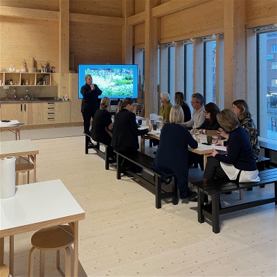 Människor som sitter vid ett bord. En person håller en presentation för de andra.