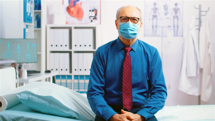En man med munskydd som sitter på en sjuksäng.