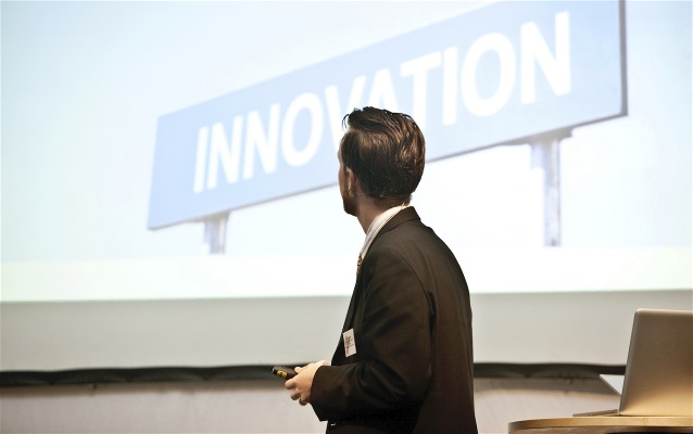Man som föreläser och tittar på skärm som visar bild med ordet "innovation"