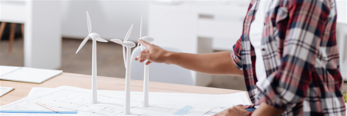 Kvinna sitter vid skrivbord med ritningar och modeller över vindkraftverk
