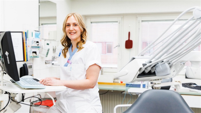 Kvinna klädd i vårdkläder i ett behandlingsrum på en tandklinik. Foto.