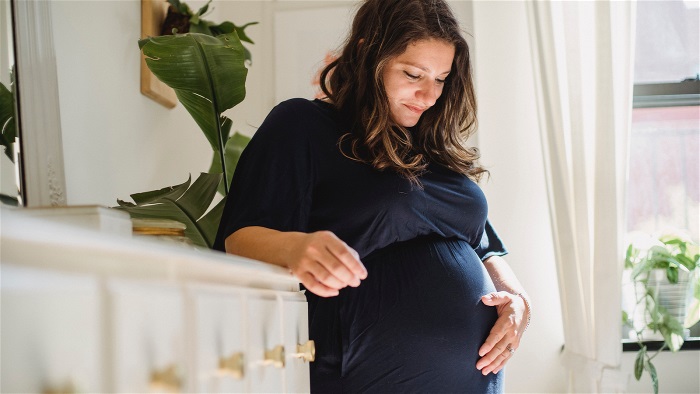 Gravid kvinna ler och håller en hand på magen.