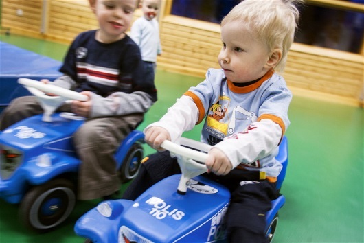 Två små barn åker på bobbycars i en gymnastikhall.